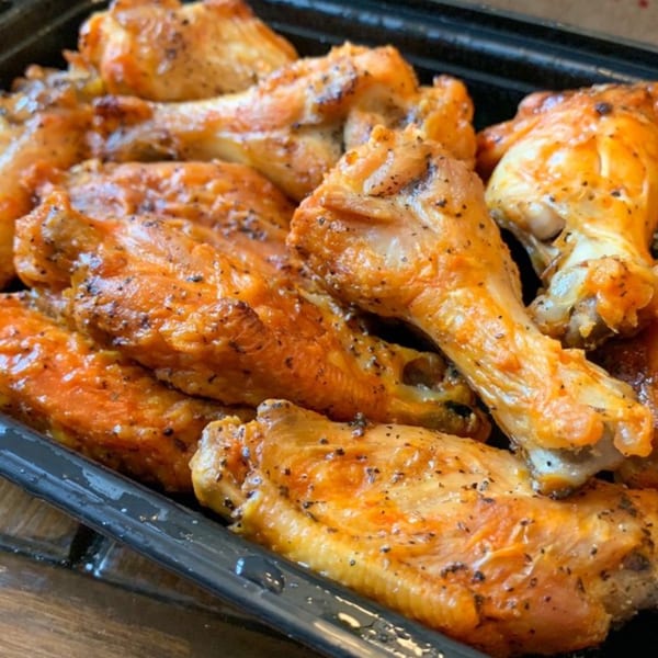 Close-up of a platter of Green Fire Pizza's golden-brown chicken wings, seasoned with black pepper.