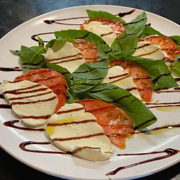Caprese salad with sliced tomatoes, fresh mozzarella, basil leaves, and balsamic glaze on a white plate.