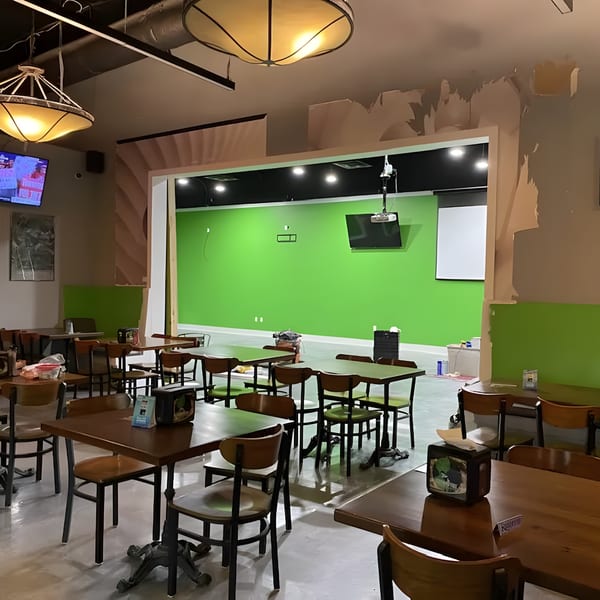 Green Fire Pizza dining area under construction with tables, chairs, and a bright green wall.