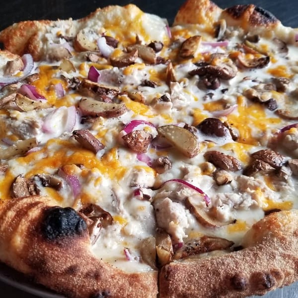 Close-up of a Green Fire Pizza with white sauce, cheese, mushrooms, potatoes, and red onions.