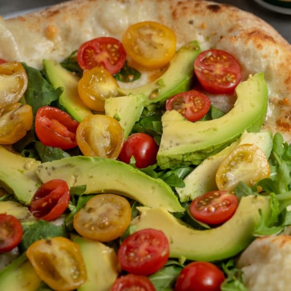 Close-up of a Green Fire Pizza with fresh avocado slices, red and yellow cherry tomatoes, and arugula.