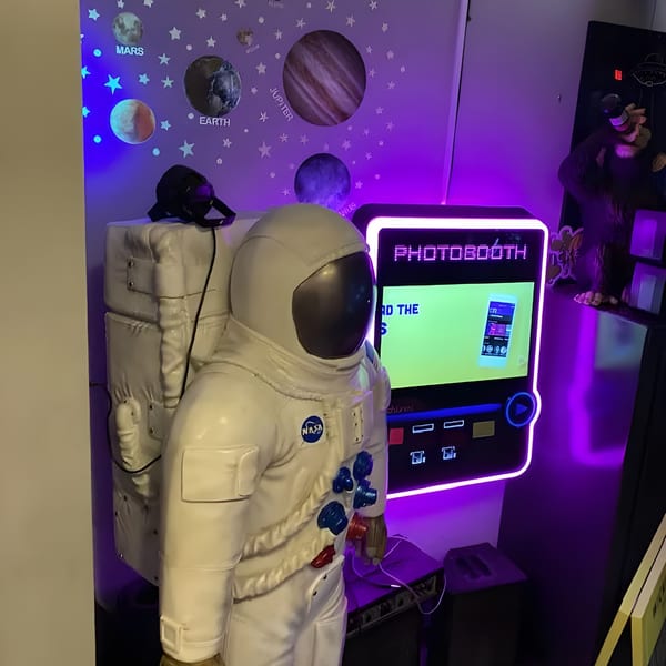A Green Fire Pizza Pooler photobooth with a life-sized astronaut statue and space-themed wall decor.