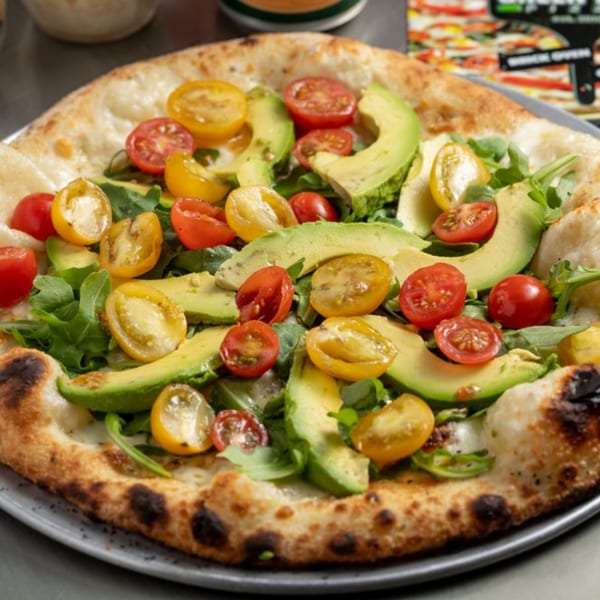 Green Fire Pizza's wood-fired pizza topped with fresh avocado slices, cherry tomatoes, and arugula.