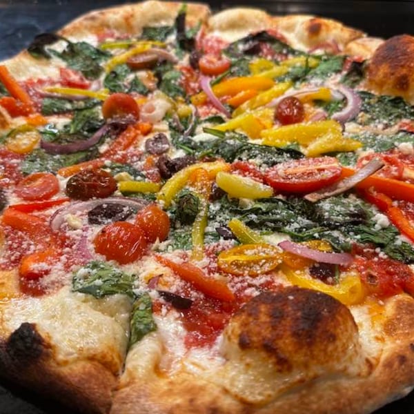 A Green Fire Pizza with colorful vegetables, including tomatoes, bell peppers, spinach, and onions.