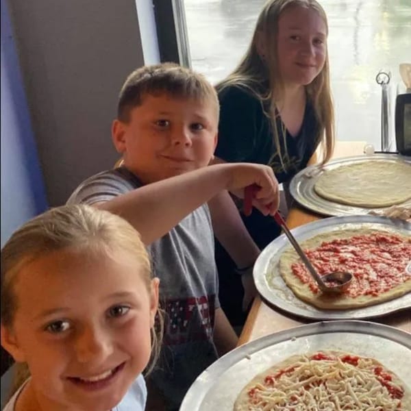 Three children making pizzas at Green Fire Pizza Pooler, with one boy spreading sauce.