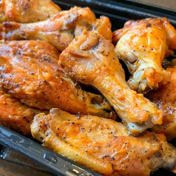 Close-up of golden-brown chicken wings seasoned with black pepper, served in a black tray.