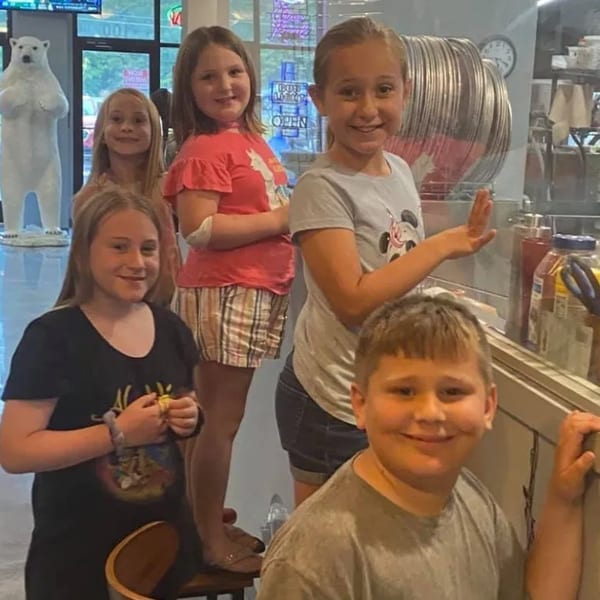 Five smiling children posing together inside Green Fire Pizza Pooler, with a polar bear statue in the background.