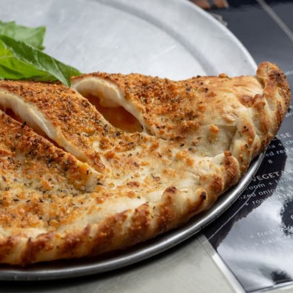 A golden-brown calzone, sliced open to reveal melted cheese, sits on a metal pizza pan.